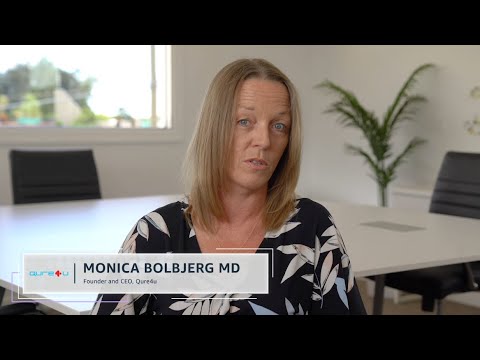 Monica Bolbjerg MD, Founder and CEO of Qure4u, speaks in an interview setting at a conference room table with visible office furnishings and a window in the background.