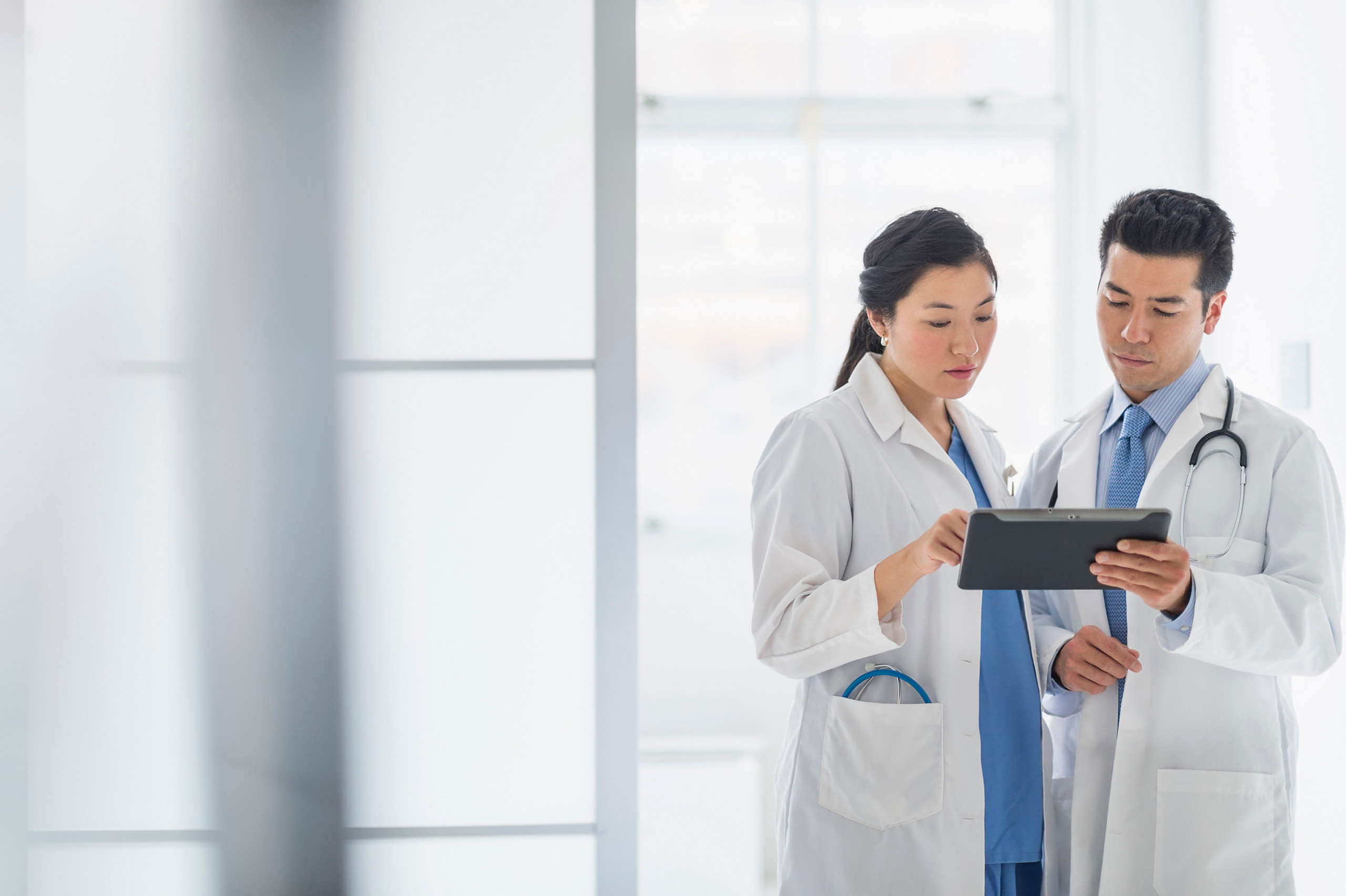 Two medical professionals in white coats are collaboratively reviewing data on a handheld tablet