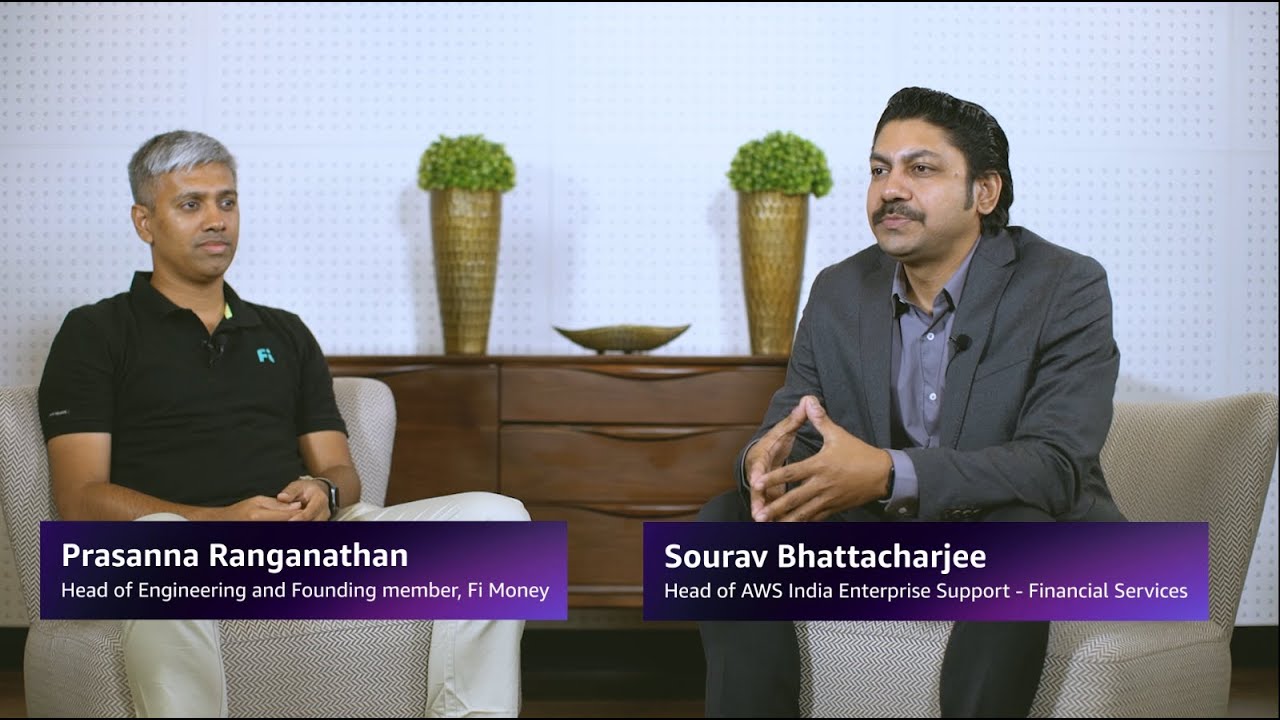 Two professionals seated for an interview: one is identified as Head of Engineering and Founding member, Fi Money, and the other as Head of AWS India Enterprise Support - Financial Services. Both are engaging in discussion in a modern business setting.