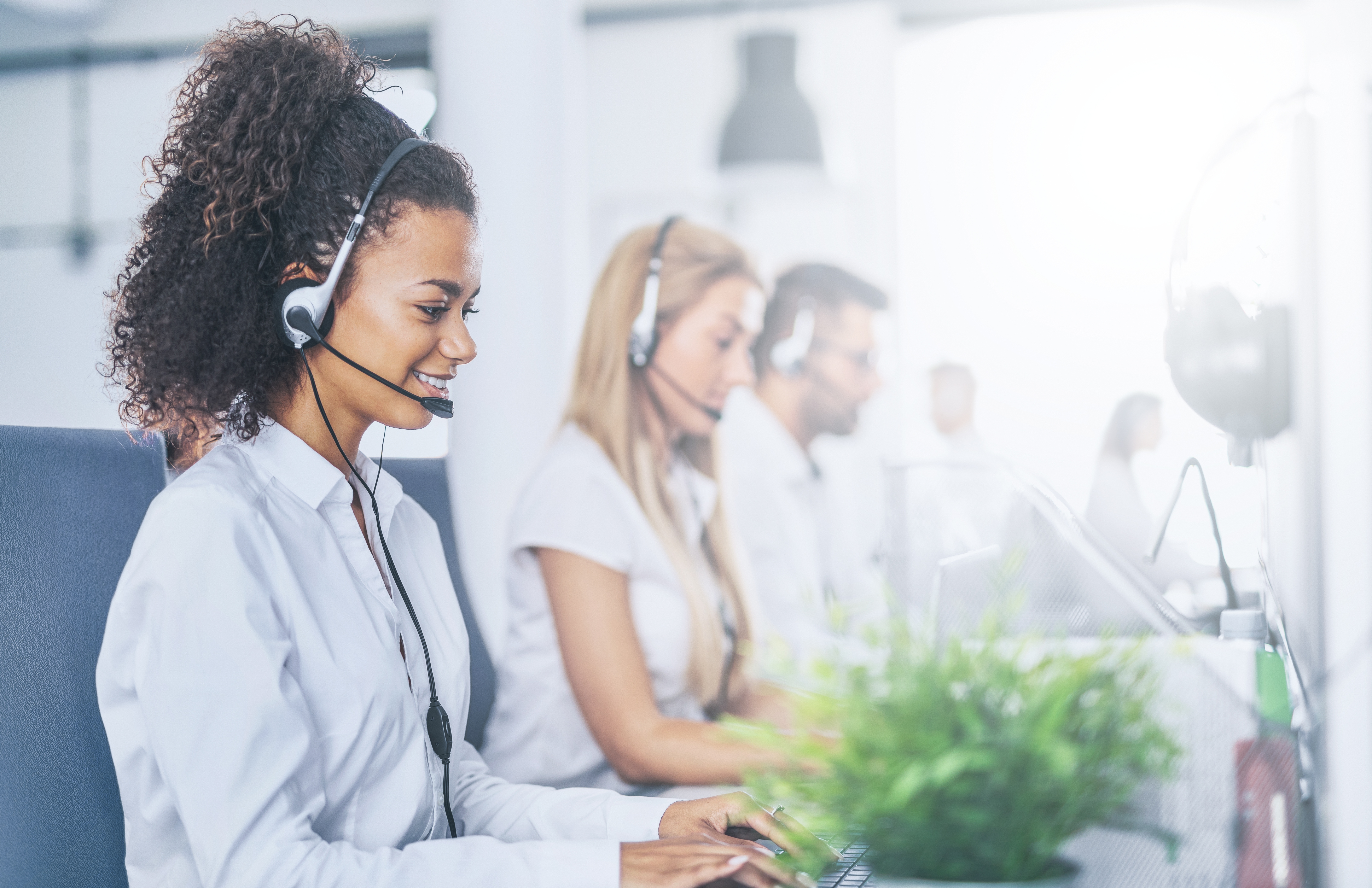 Customer service representatives working at computers while wearing headsets, providing support in a bright modern office environment.