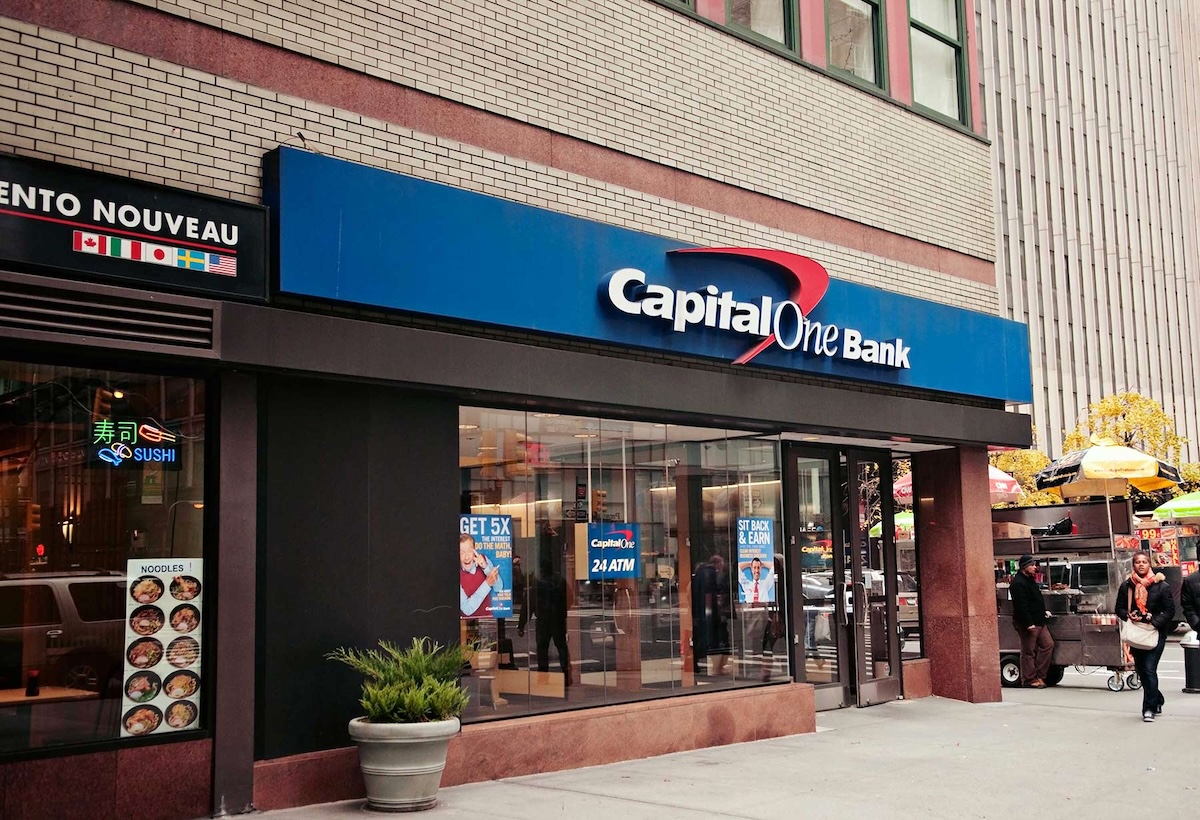 Capital One Bank storefront on a city street, next to a sushi restaurant and a food cart.