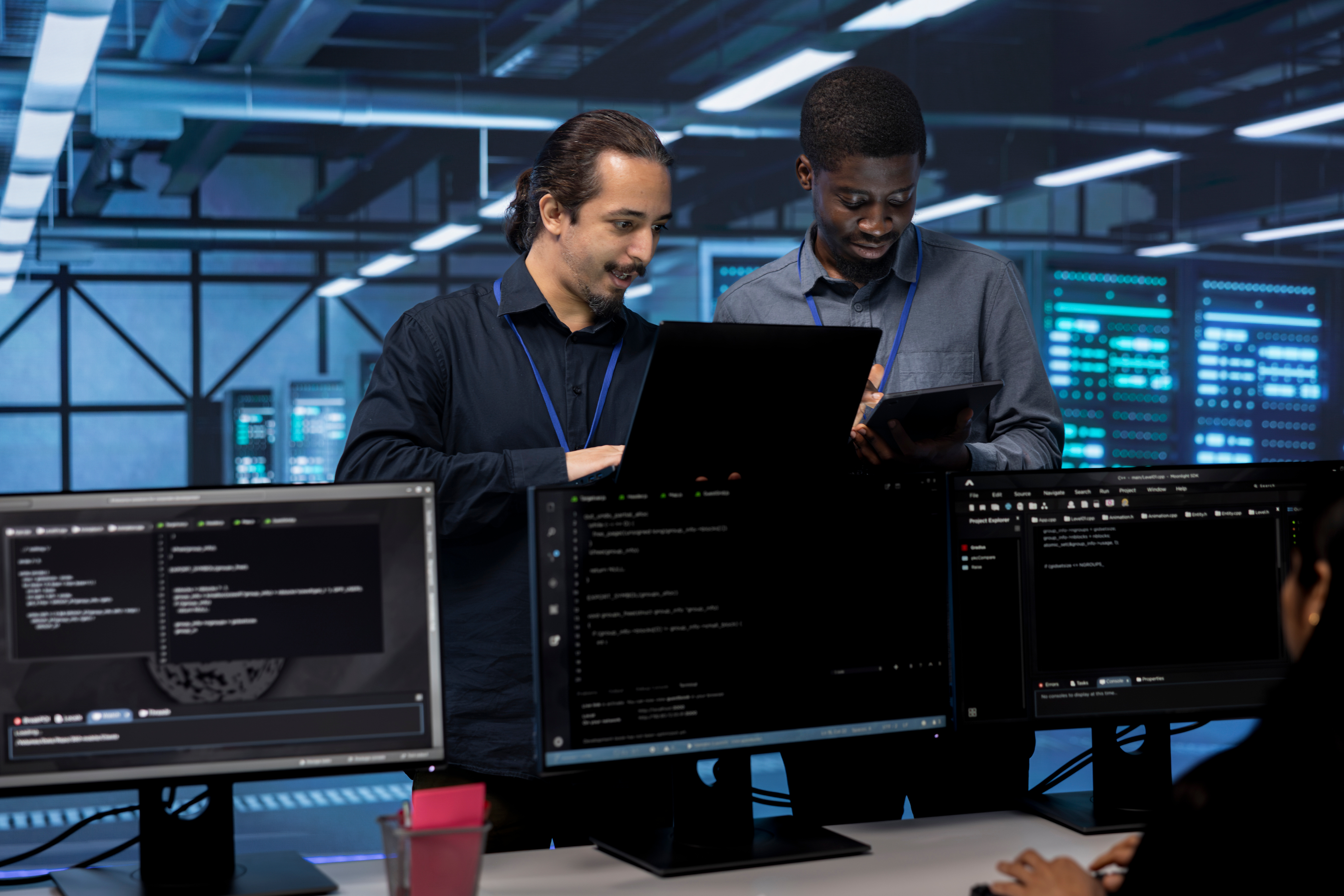 Coworkers in data center using laptop and tablet to find firewall misconfigurations affecting servers. Colleagues in server room checking systems bottlenecks leading to sluggish data transfer rates