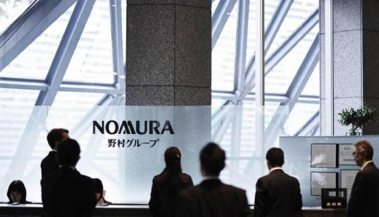 People in business attire standing near a reception area with the "Nomura" logo and Japanese text on a glass panel, set against a modern architectural backdrop.