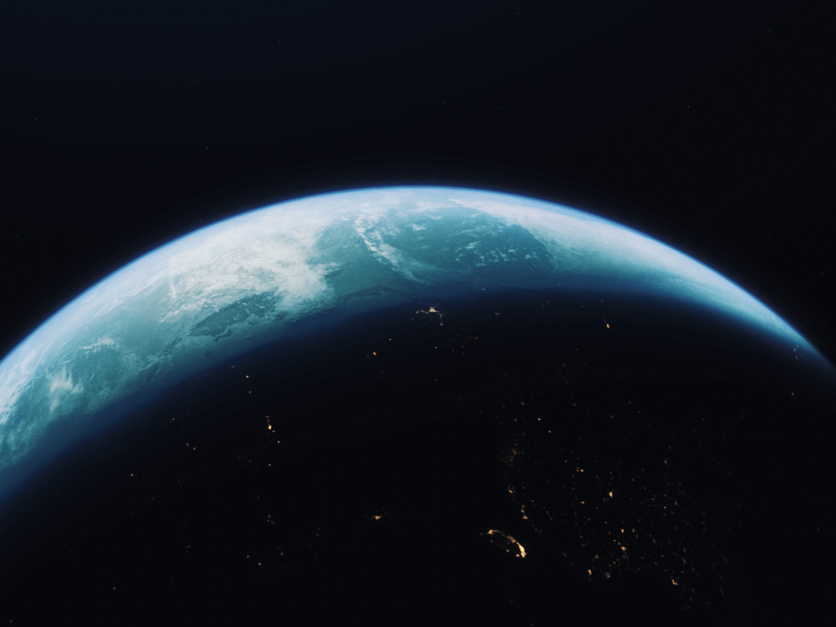 View of Earth from space, showing a glowing atmosphere and illuminated city lights on the dark surface.