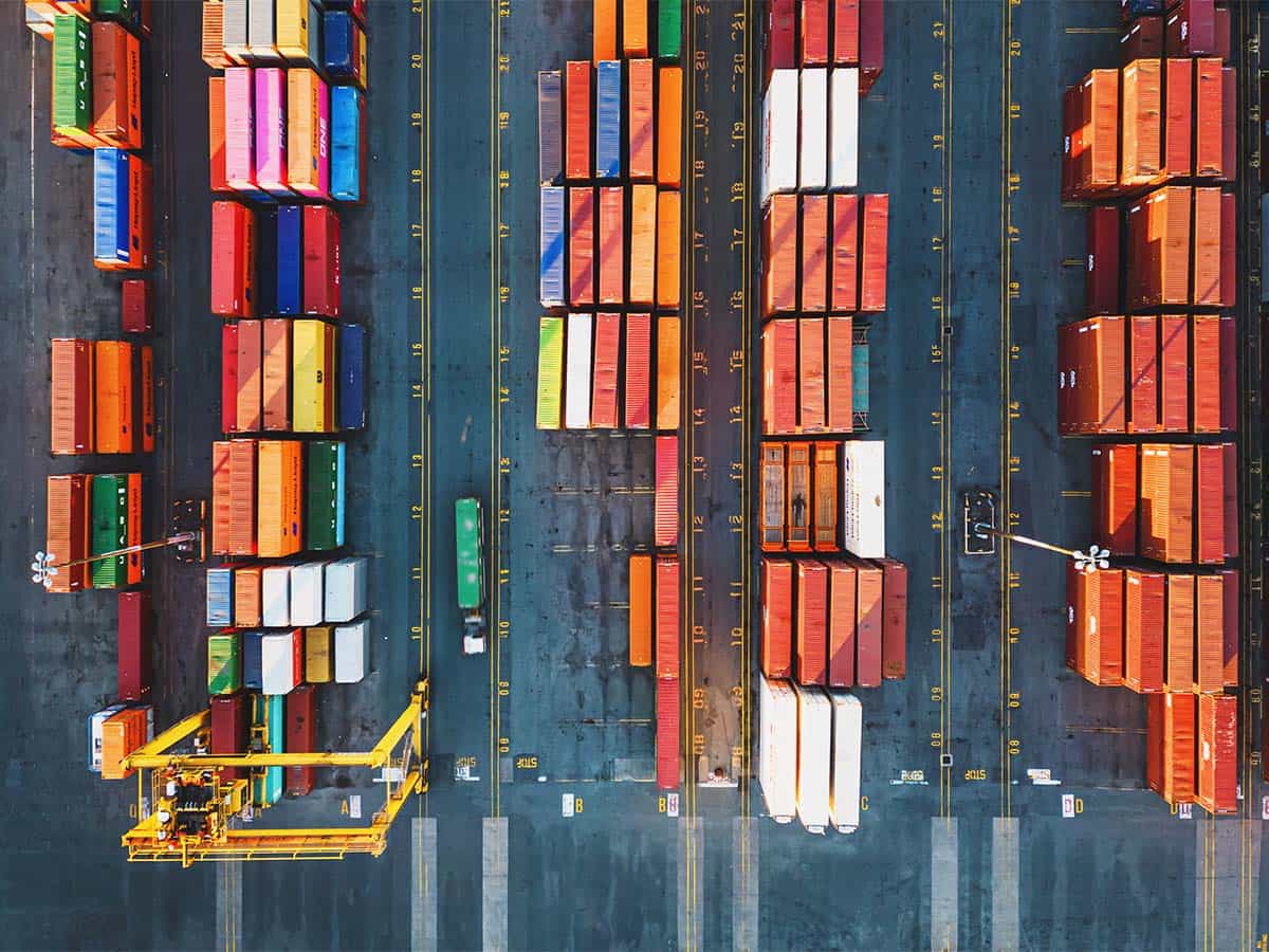 Aerial view of colorful shipping containers arranged in rows at a port, with a container crane and transport vehicles visible.