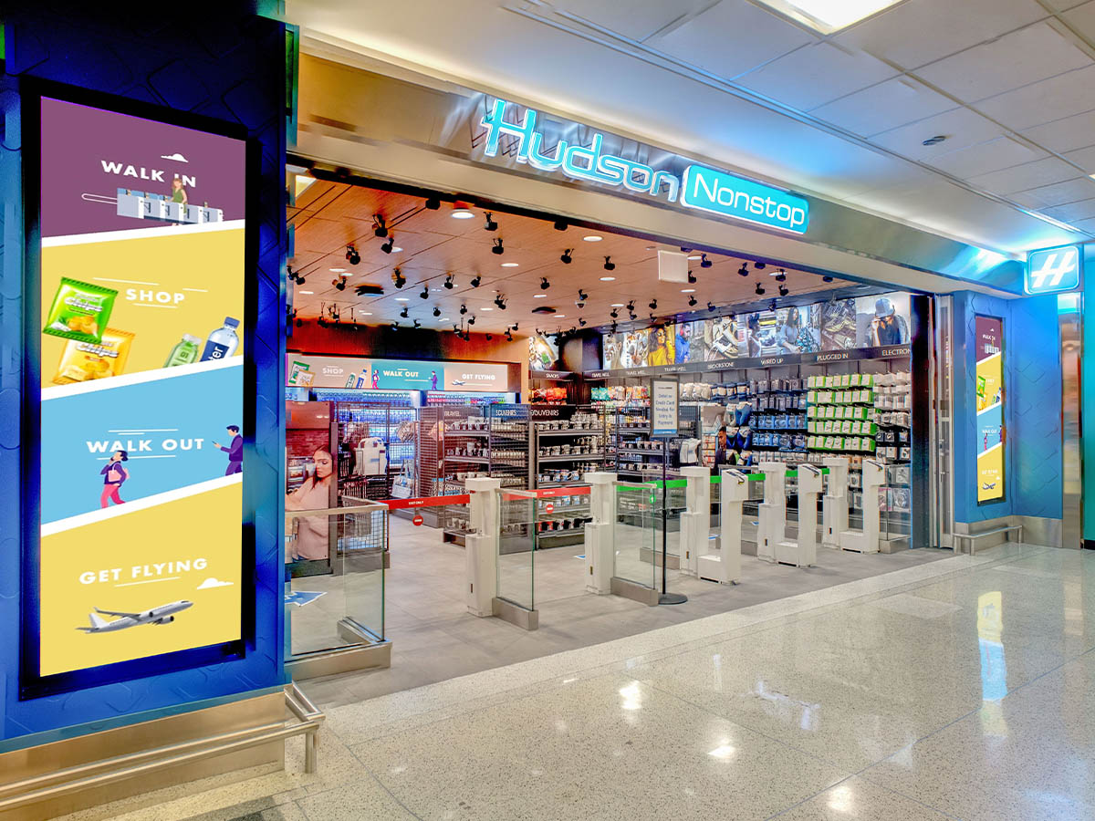 The exterior of a Hudson Nonstop grab-and-go convenience store located inside an airport, featuring automated entry gates, displays of travel essentials, and illustrated signage inviting travelers to walk in, shop, and walk out quickly before their flights.