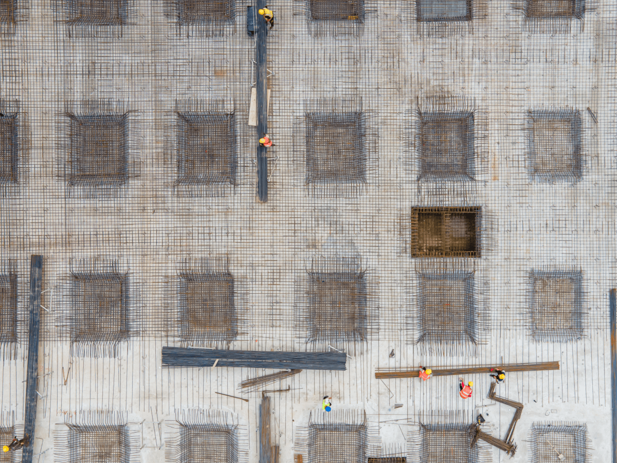 Aerial view of a construction site showing a concrete foundation grid, rebar structures, and several workers in safety gear working on the site.