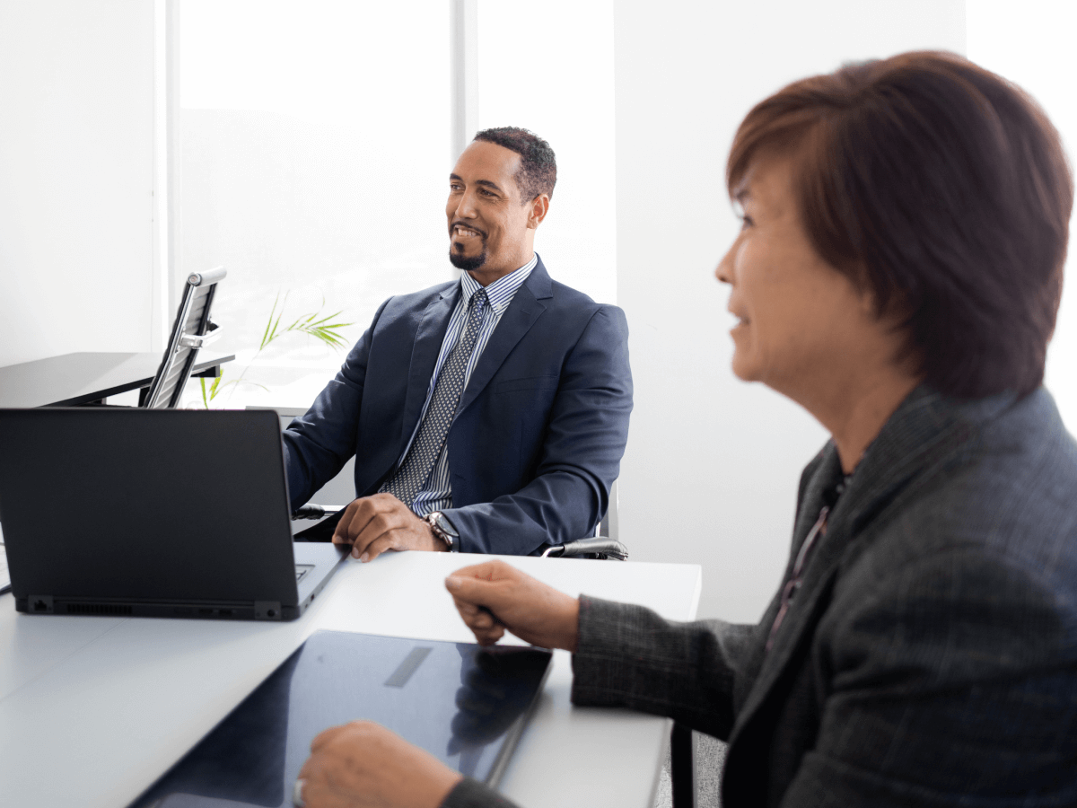 Two business professionals having a meeting in a modern office setting, with laptops on the table.