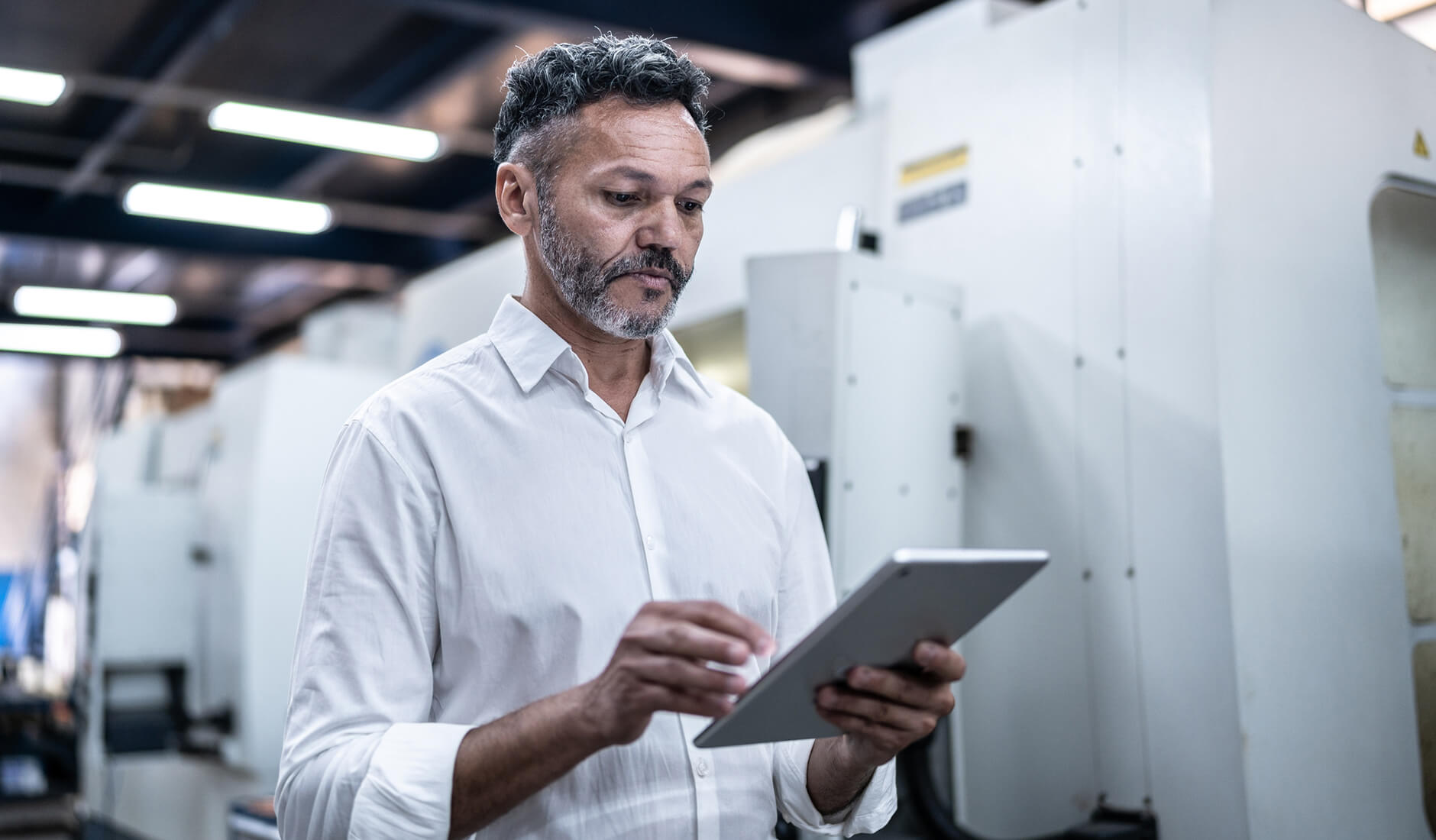 A man in a white shirt using a tablet in an industrial or manufacturing workplace environment.