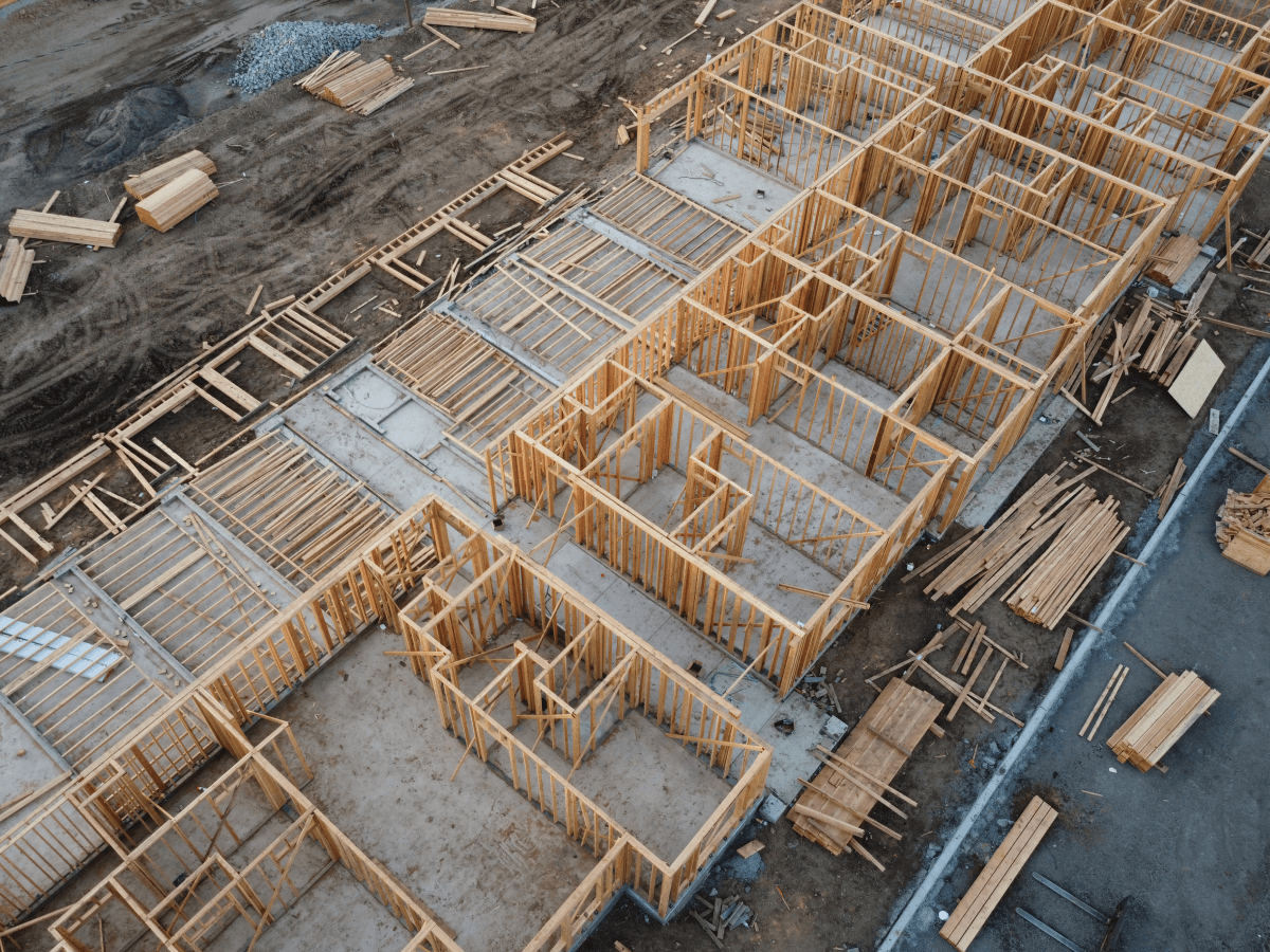 Aerial view of the wooden framing stage of residential home construction, showing the layout of multiple units and scattered building materials on a construction site.
