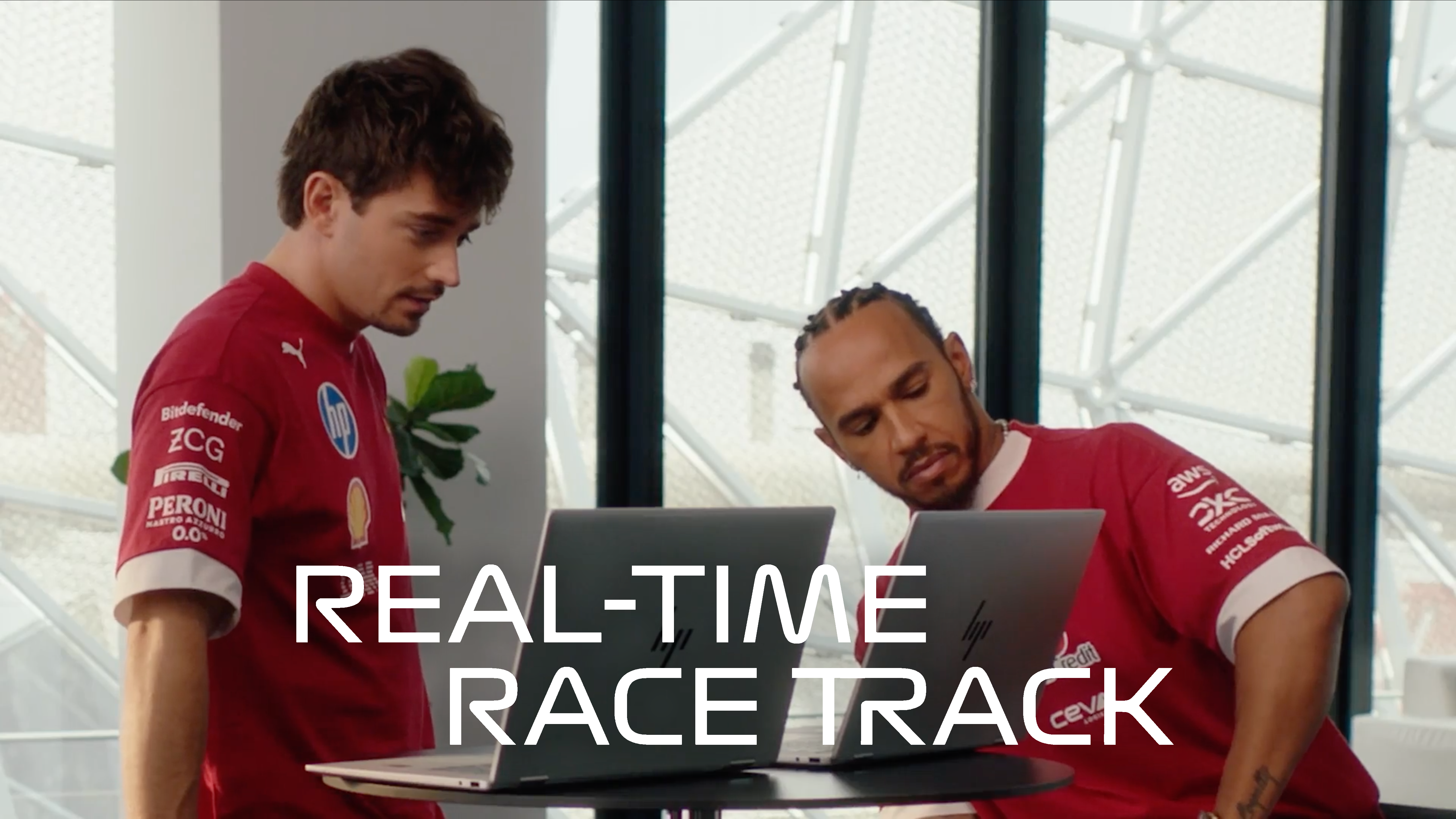 Two people in red team uniforms working on laptops with "Real-Time Race Track" text overlay.