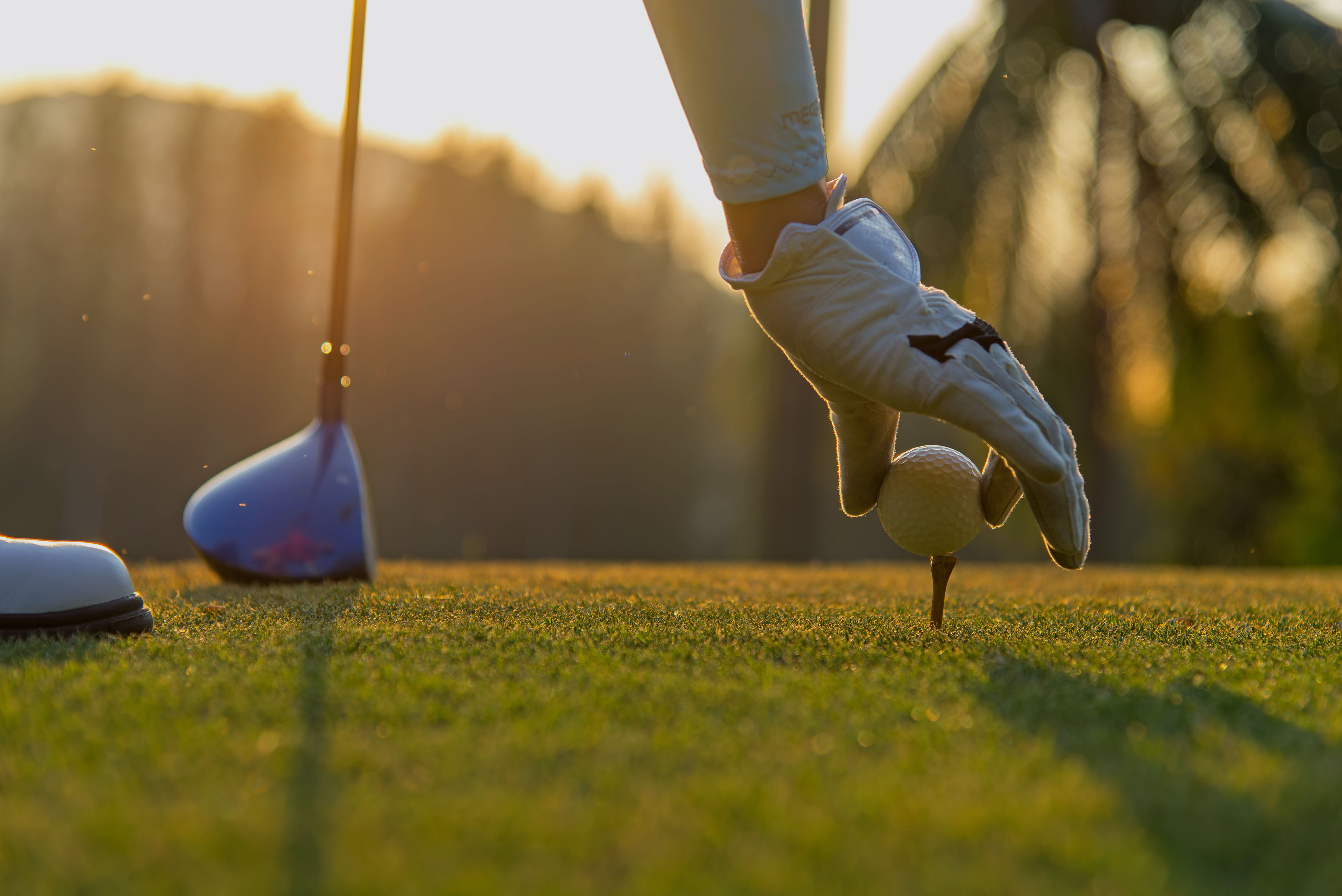 Hand asian woman putting golf ball on tee with club in golf course on evening and sunset time a for healthy sport.  Lifestyle Concept
