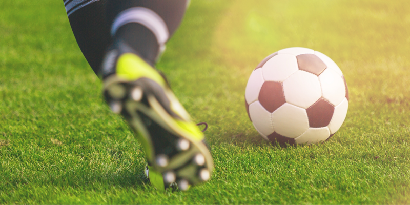 A soccer player kicking a black-and-white soccer ball on a grassy field.
