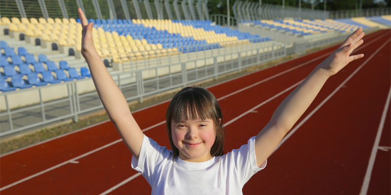 A person raising their arms on a red running track with empty stadium seating in the background.