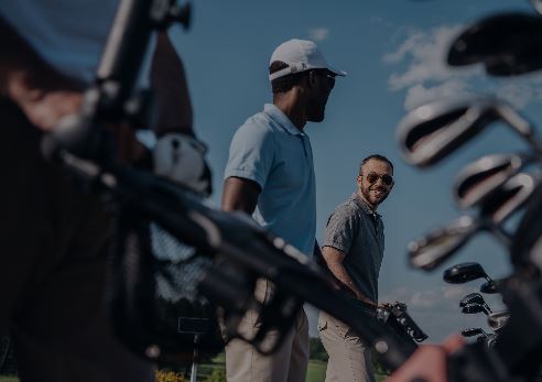 Golfers standing outdoors near golf bags under a clear blue sky.