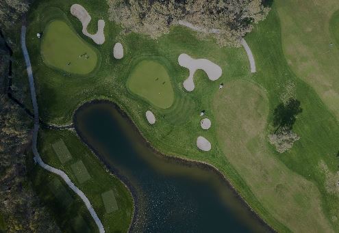 Aerial view of a golf course featuring greens, sand bunkers, a pond, and surrounding grass.