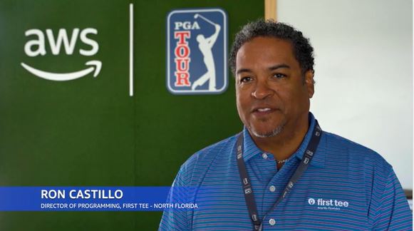 Ron Castillo, Director of Programming for First Tee - North Florida, wearing a blue polo with logos, stands in front of AWS and PGA Tour branding.