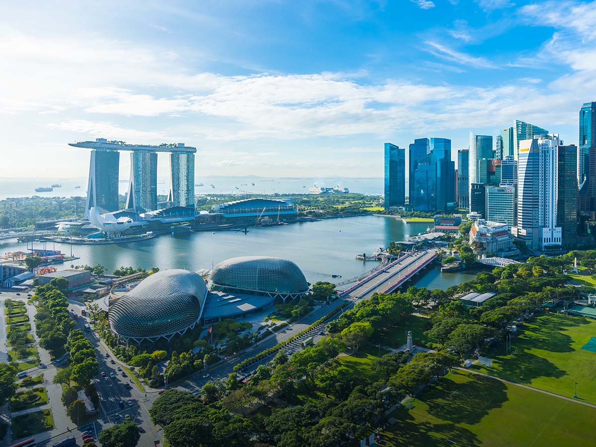 Aerial view of Singapore Marina Bay skyline, featuring Marina Bay Sands, Esplanade Theatres, and modern skyscrapers against a blue sky.