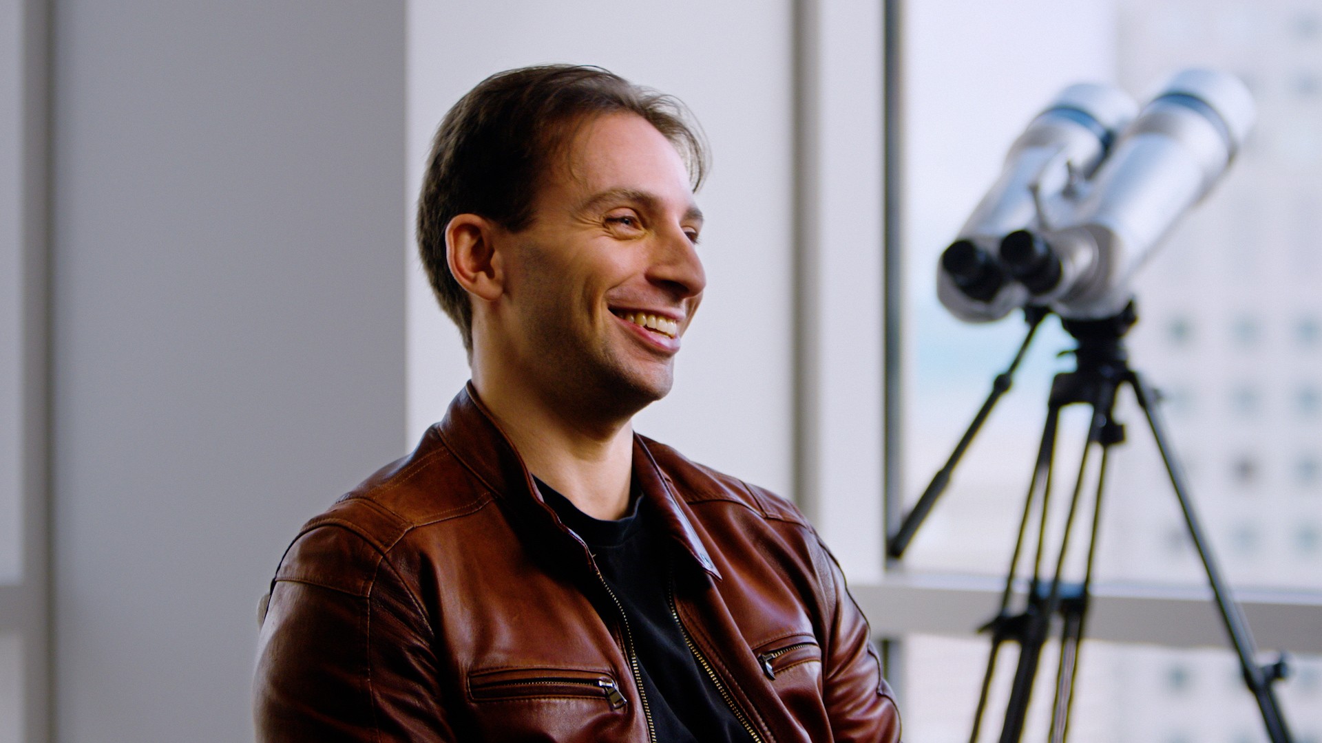 Smiling startup founder looking through a telescope-style camera, illustrating the It starts with AWS section.