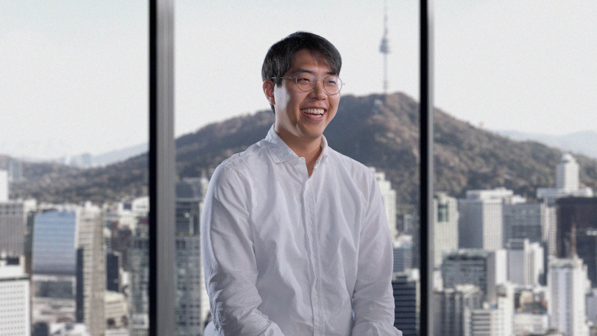 Roi Nam, CEO of AB180, smiling in a white shirt with a Seoul city view behind him