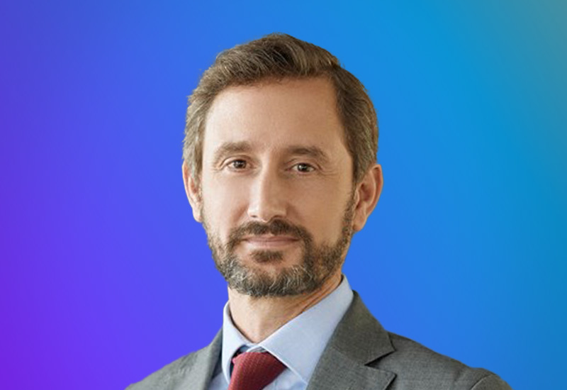 Professional headshot of a man in a suit with a beard, set against a blue and purple gradient background, used for the Madrid Summit event.