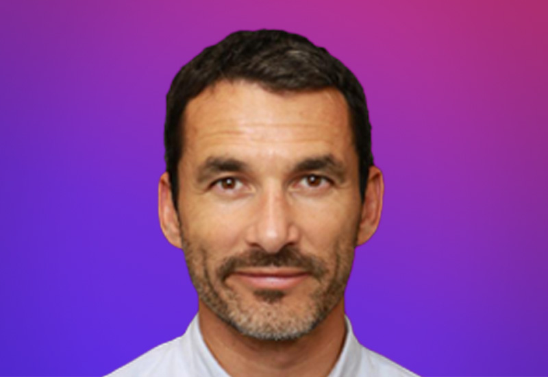 Professional headshot of a man in front of a purple and pink gradient background, used for the Partner Summit in Paris.