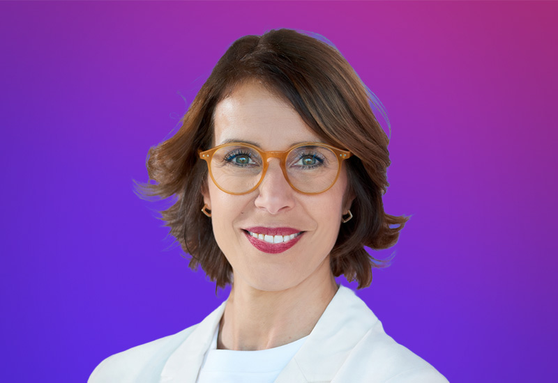 Professional headshot of a woman with short brown hair and glasses, set against a vibrant pink and purple gradient background, taken for the AWS Partner Summit Madrid event.
