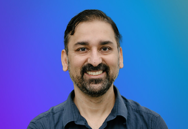 Professional headshot photo featuring a smiling person posed against a blue to purple gradient background, used for AWS Summit Madrid event materials.