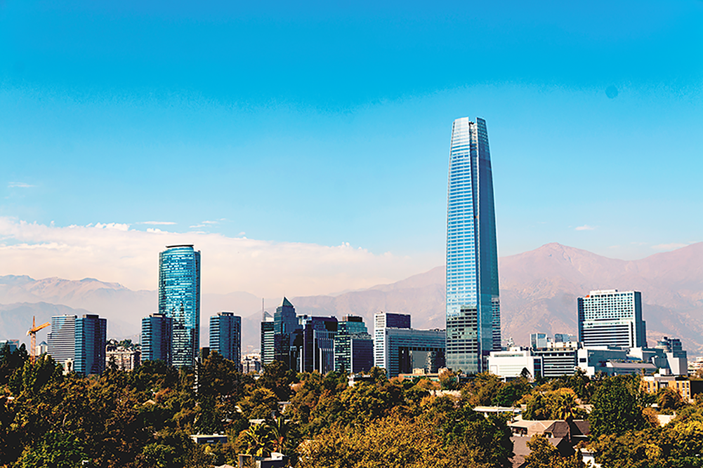A cityscape of Santiago, Chile, featuring modern skyscrapers and the Andes mountains in the background under a clear blue sky.