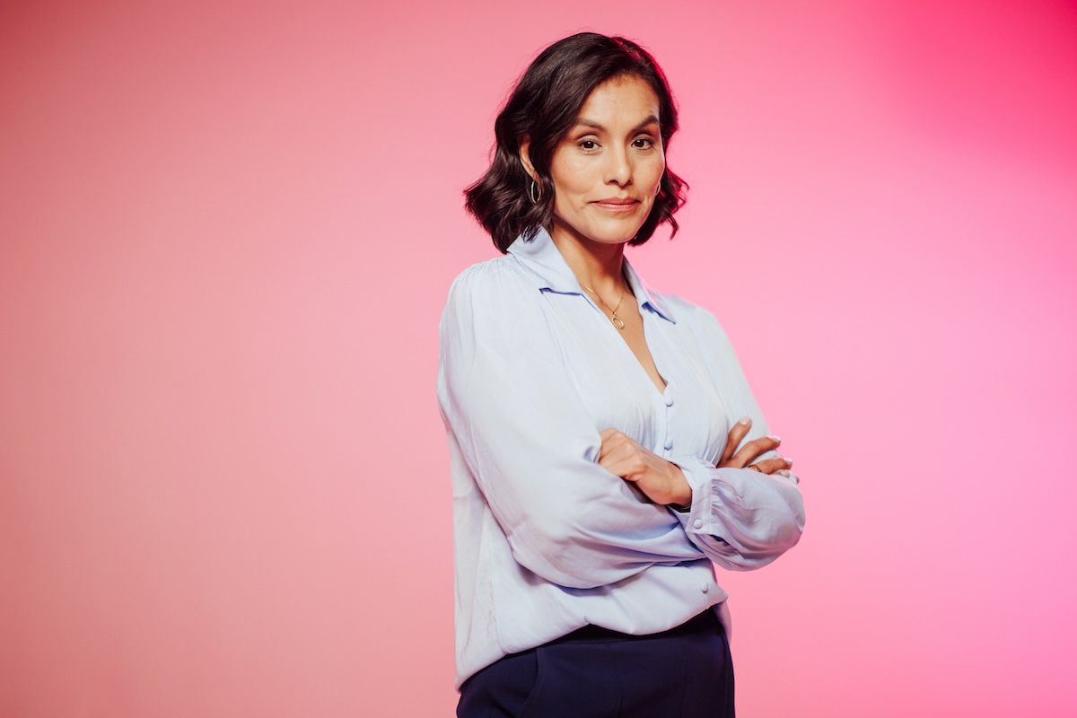 Portrait of a woman standing with arms crossed against a pink background