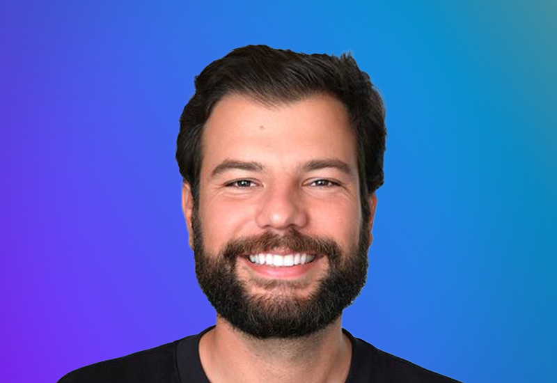 Portrait of a smiling man with a beard, photographed against a blue to purple gradient background.