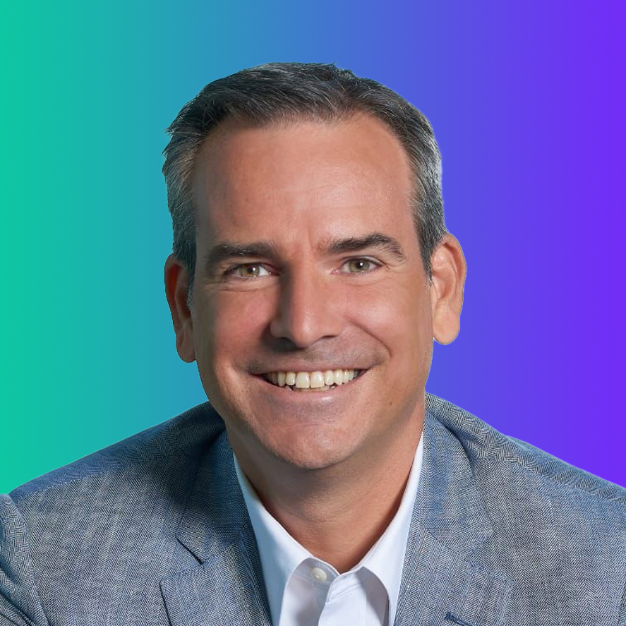 A professional headshot of a man smiling, wearing a light blue suit jacket and white shirt, set against a blue-to-purple gradient background.