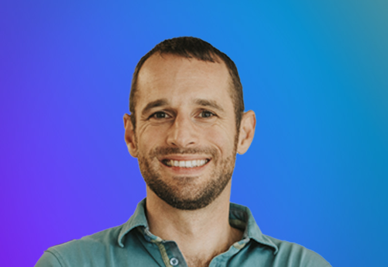 A man smiling in front of a blue and purple gradient background.