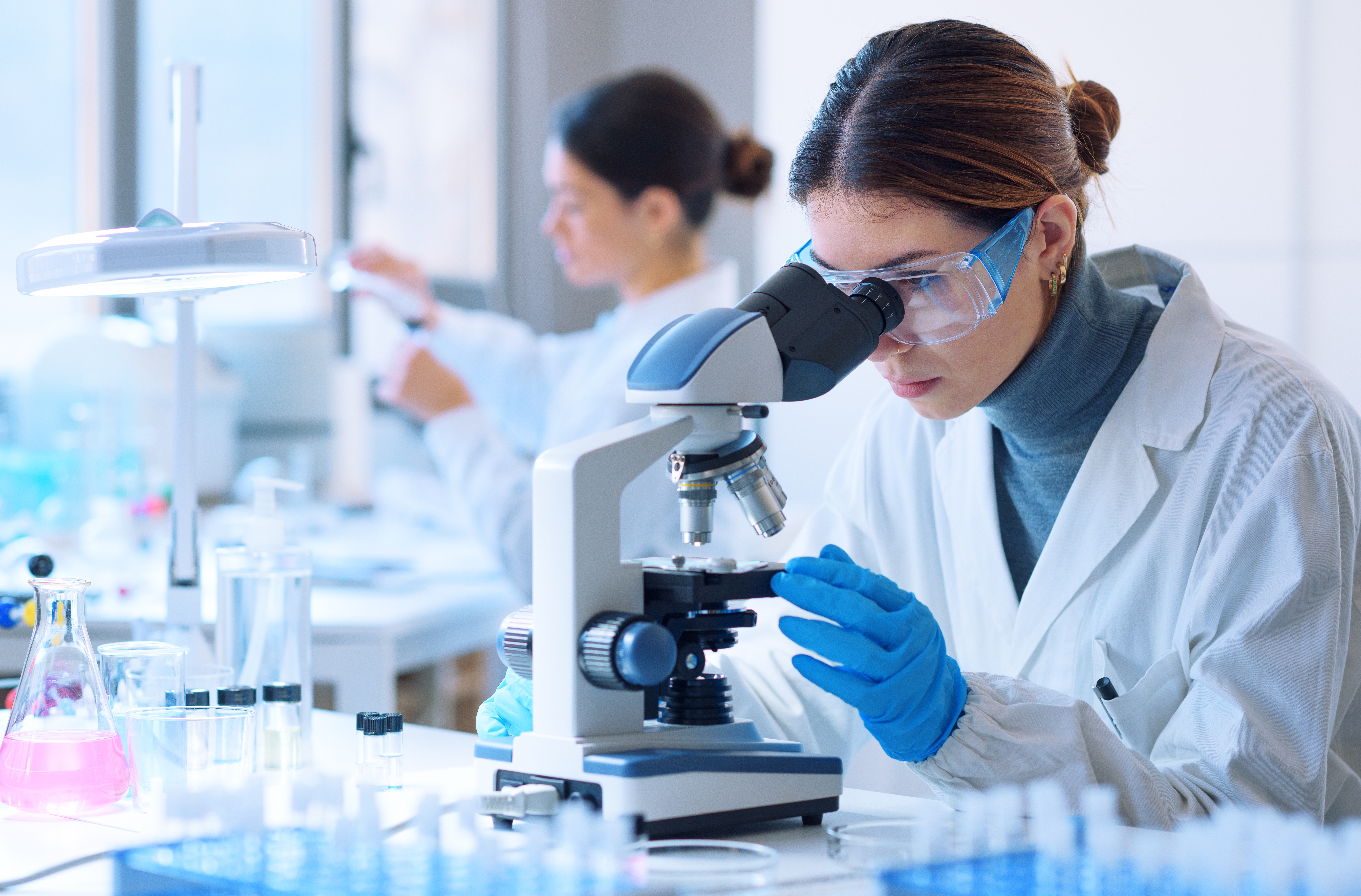 Young scientists conducting research investigations in a medical laboratory, a researcher in the foreground is using a microscope; Shutterstock ID 2149947783; purchase_order: OneBio case study; job: AWS; client: case study; other: EMEA