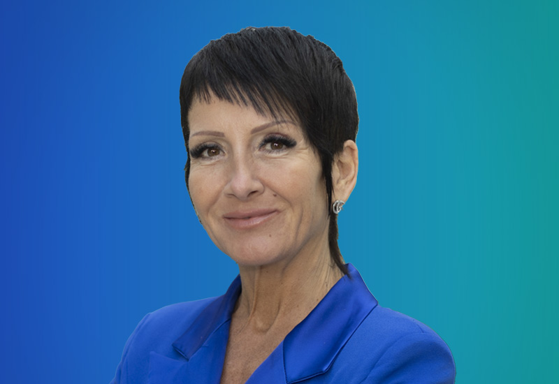 Professional headshot of a woman with short, dark hair wearing a blue blazer, posed in front of a blue gradient background.