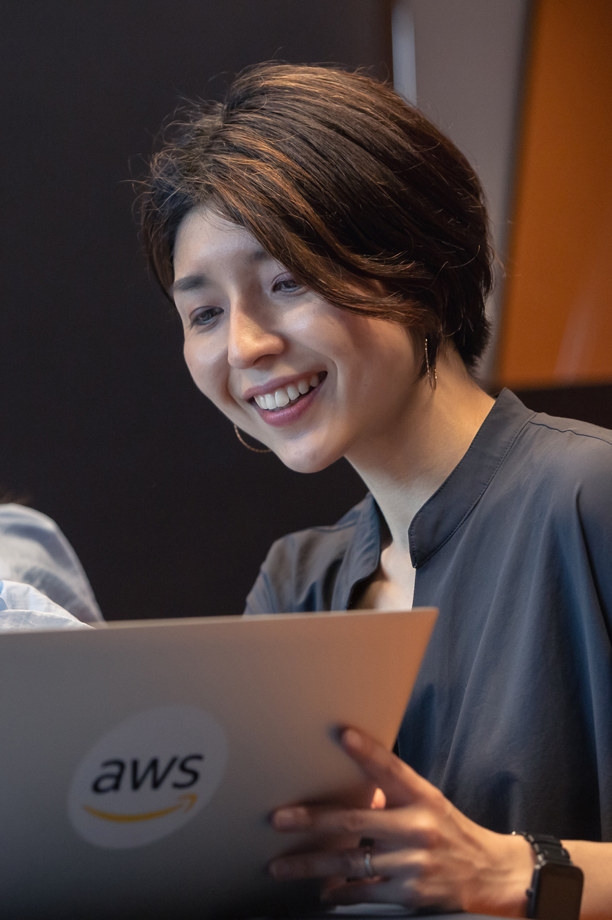 An AWS employee smiling while working on a laptop with an AWS logo.
