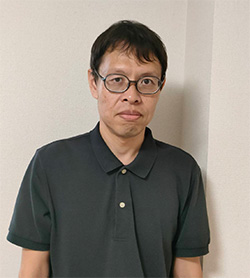 Profile photo of Matsui Takahiro wearing glasses and a dark polo shirt, standing against a light-colored wall.