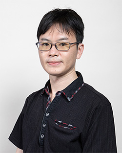 A professional portrait of Shiraishi Takuya, wearing glasses and a dark collared shirt, posed against a plain light background.