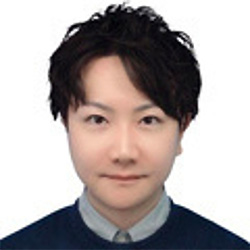Profile headshot of an individual with short dark hair, wearing a collared shirt and sweater, photographed against a plain white background.