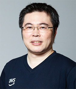Portrait of an individual wearing glasses and an AWS shirt, photographed in a studio setting with a plain background.