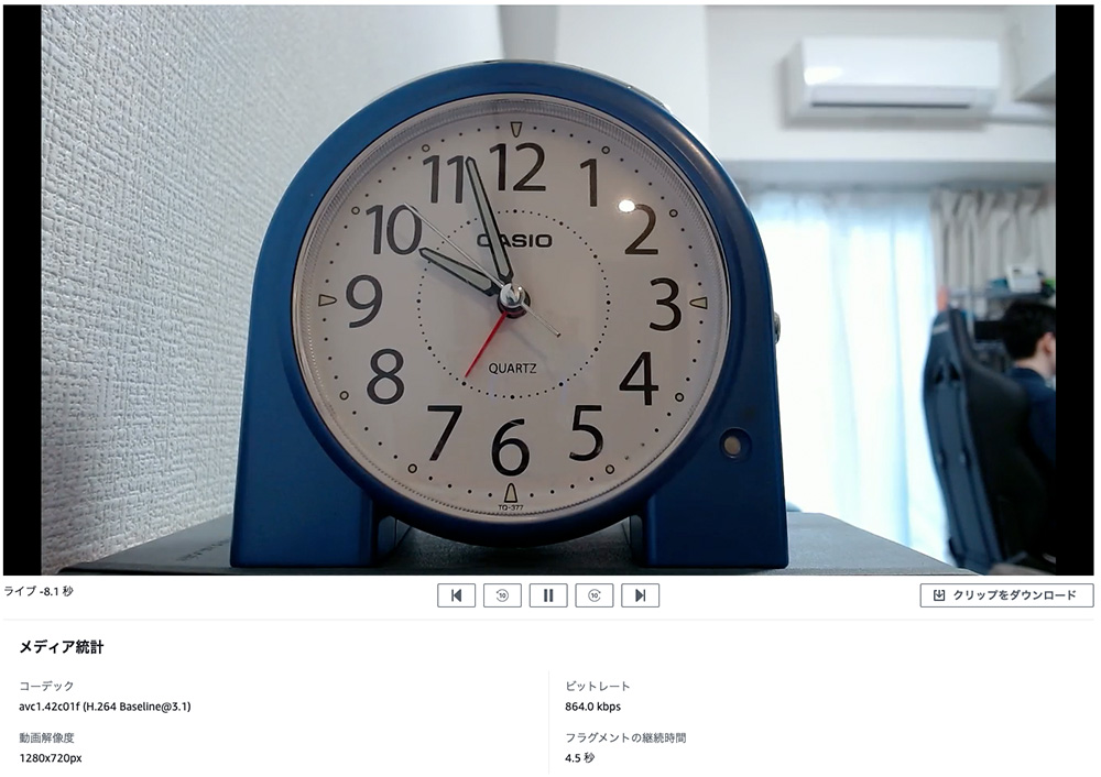 A blue Casio analog clock is displayed in the foreground, shown in a time lapse video interface. The setting appears to be an indoor room, with a desk and chair visible in the background. The image includes media playback controls and technical details in Japanese text at the bottom.