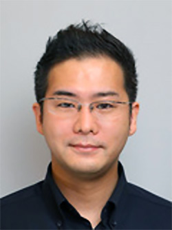A professional headshot portrait of a man with short black hair, glasses, and a dark shirt, set against a neutral background.