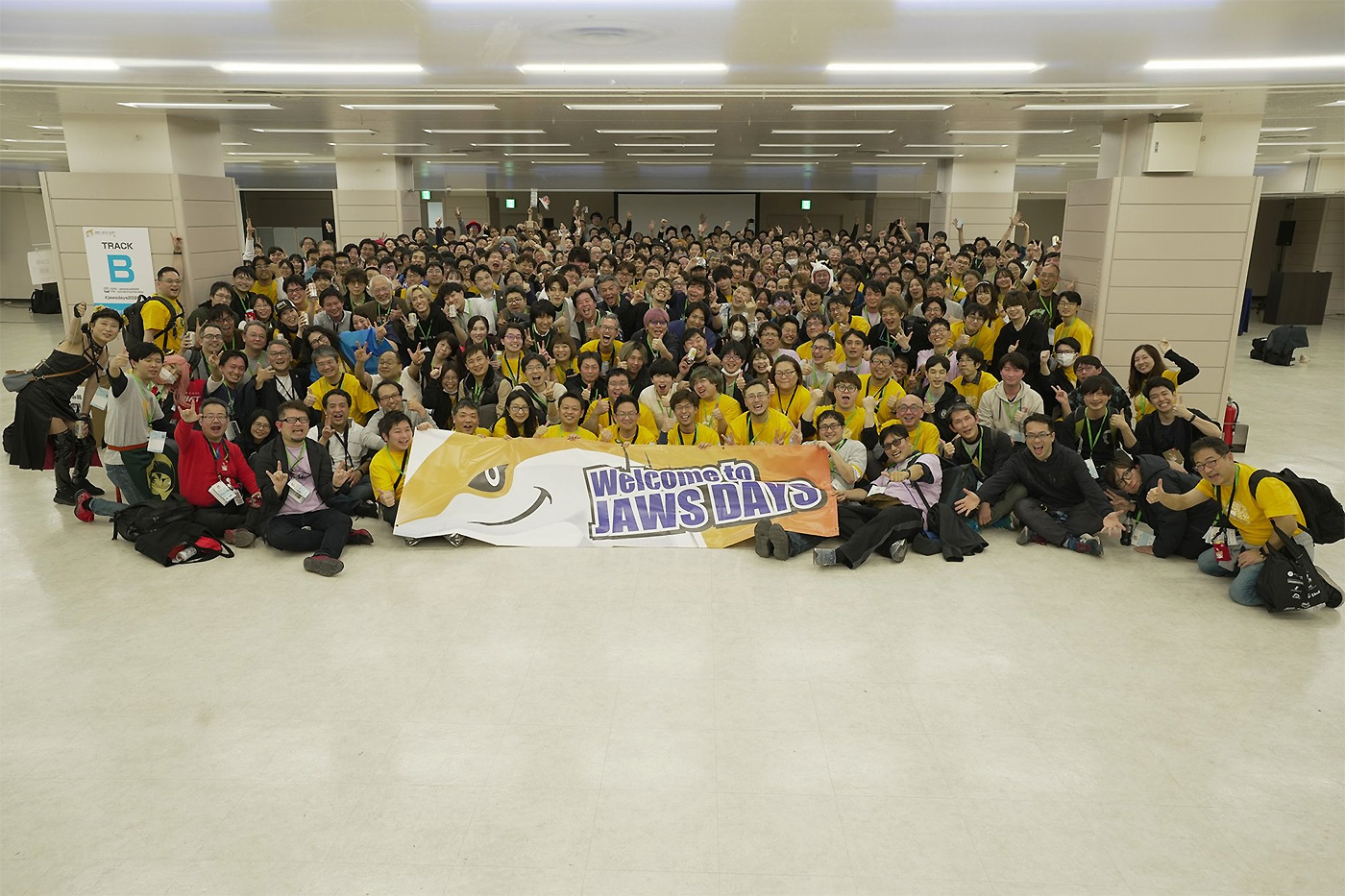 Large group photo of attendees at JAWS DAYS 2024, gathered indoors and holding a 'Welcome to JAWS DAYS' banner.
