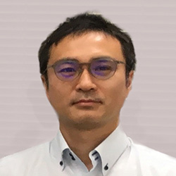 Portrait of a man wearing glasses and a collared shirt, against a light background.