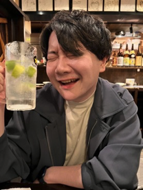 A person smiling and holding a drink with lime at a restaurant table.