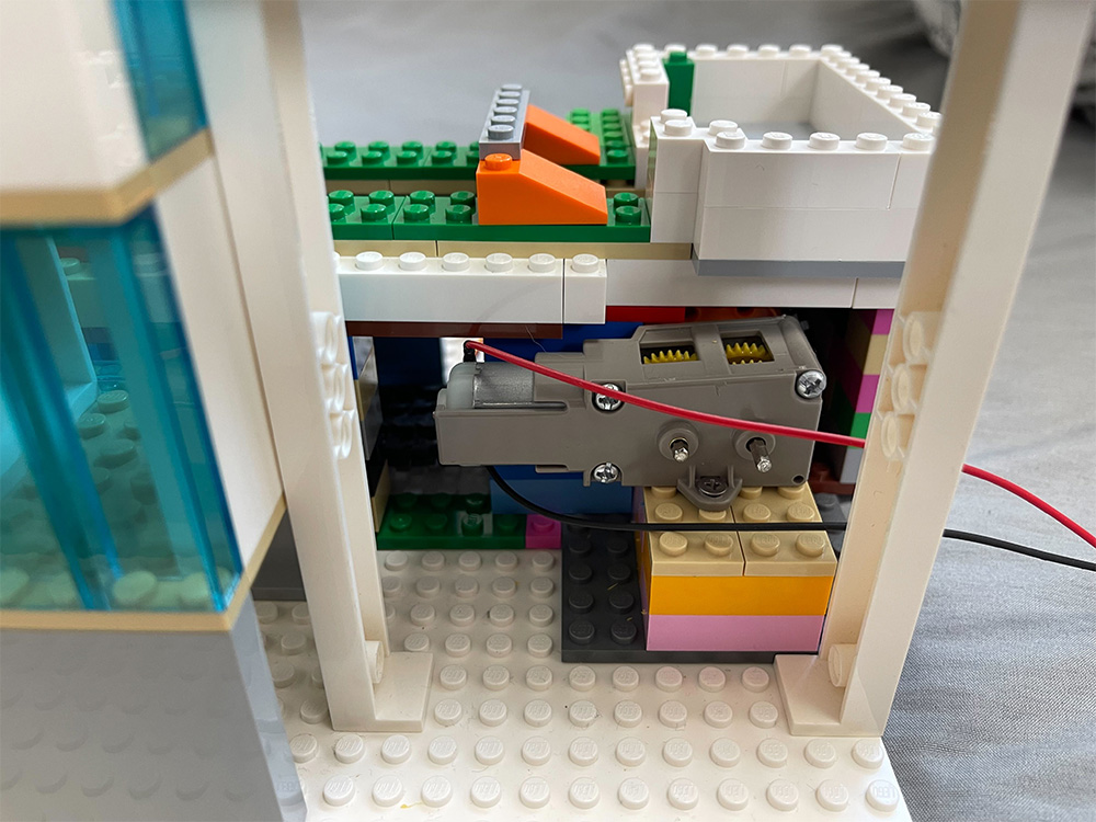 A detailed closeup of the internal wiring and motor mechanism inside a colorful LEGO model, showing gears, wires, and bricks assembled together.