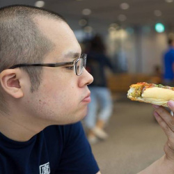 A man wearing glasses is eating a hot dog indoors.