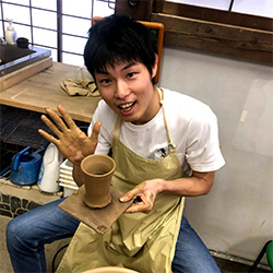 A person participates in a pottery workshop, smiling while shaping clay on a pottery wheel.