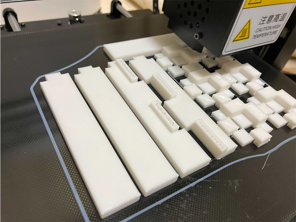 A 3D printer in operation, producing multiple white plastic parts on its build platform.