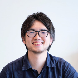 A smiling man with glasses and a casual dark shirt, facing the camera against a plain background.